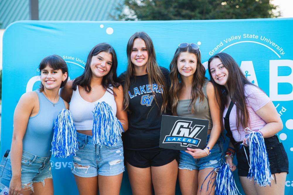 five people posing in front of CAB backdrop at Laker Kickoff photo booth and holding GV sign and blue and white pom poms